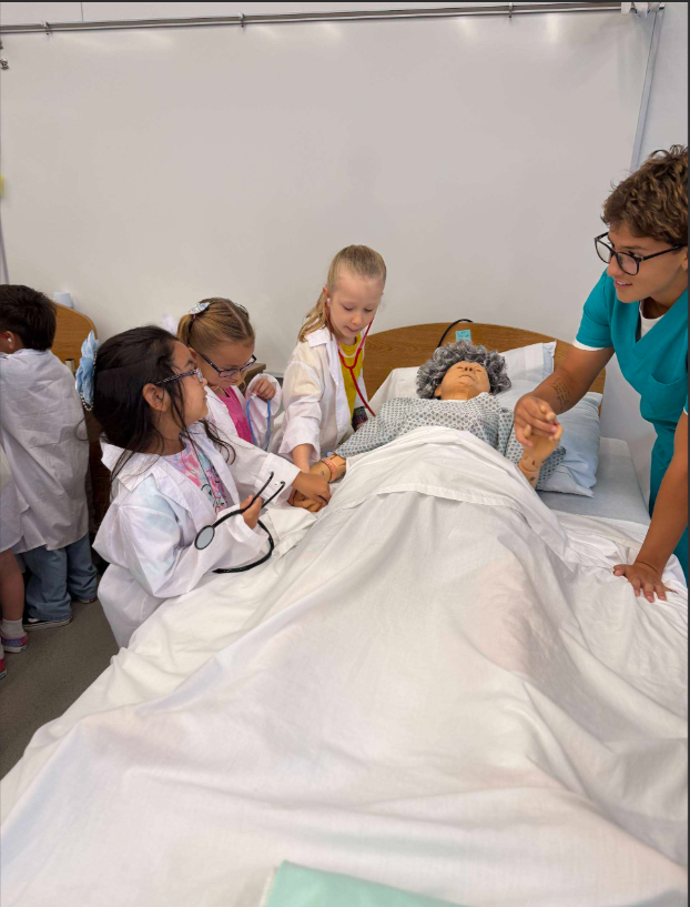 A group of children dressed as medical professionals examining a patient lying in a hospital bed
