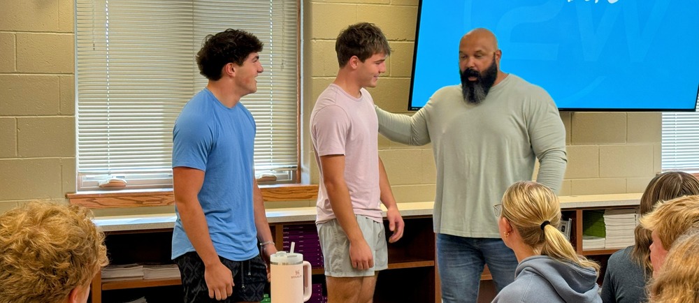 Stephen Mackey standing with two students in front of classroom during presentation on leadership