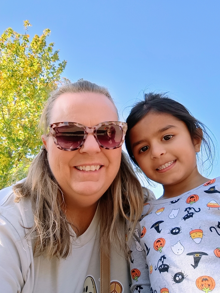 Two people posing for a selfie. A young student and teacher. There is a tree in the background and. a blue clear sky.