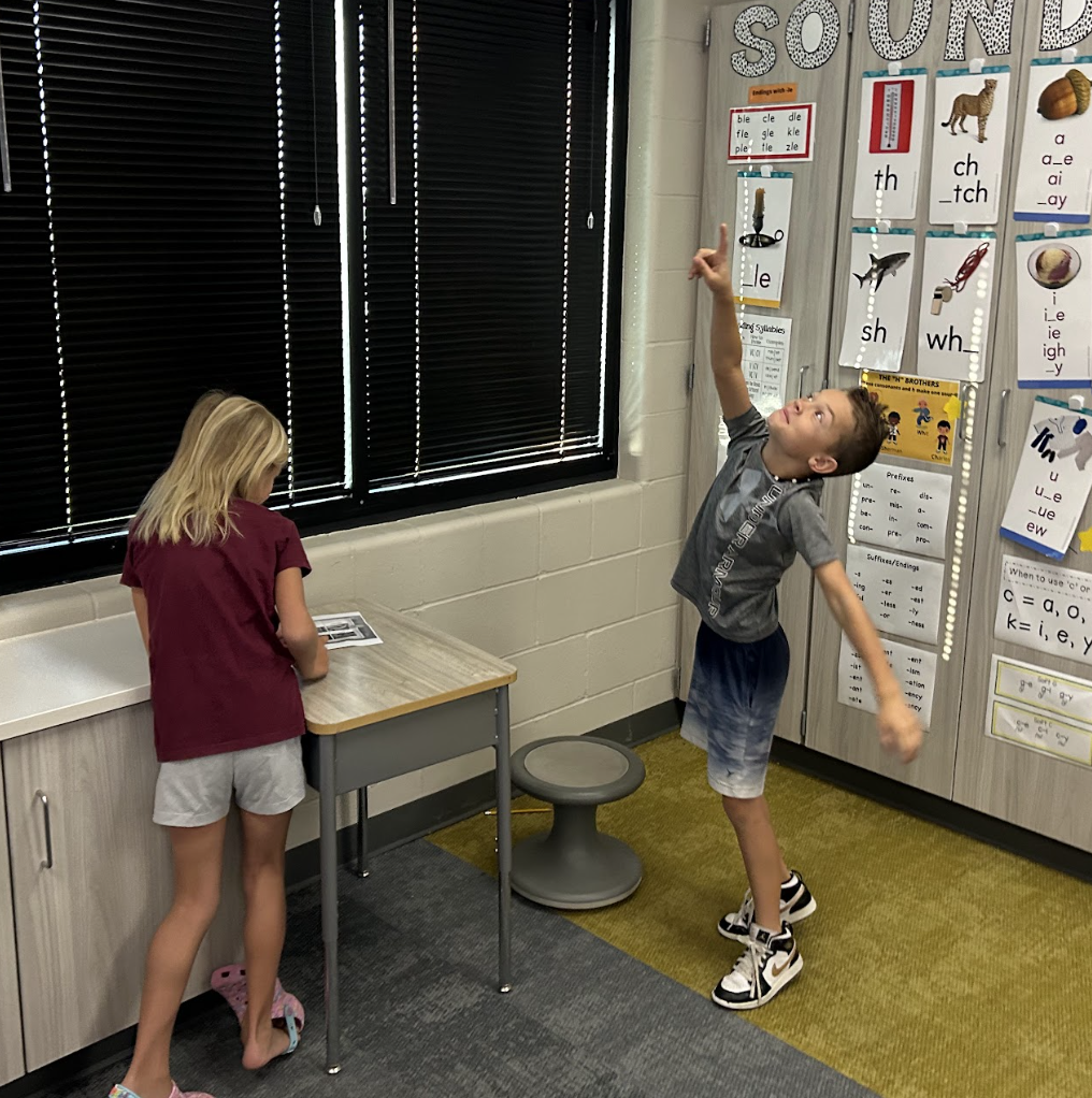 two students act out a story from a book in the clasroom.