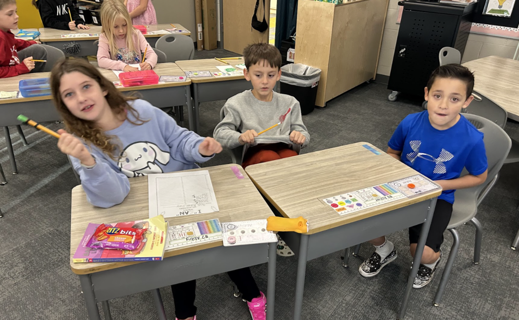 three students at desks with books and worksheet