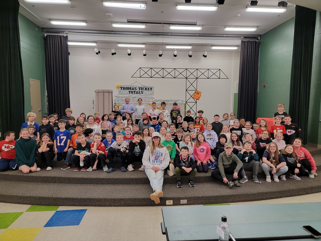 3rd grade students seated on the stage alongside Supernova volleyball player Mac Padraza.