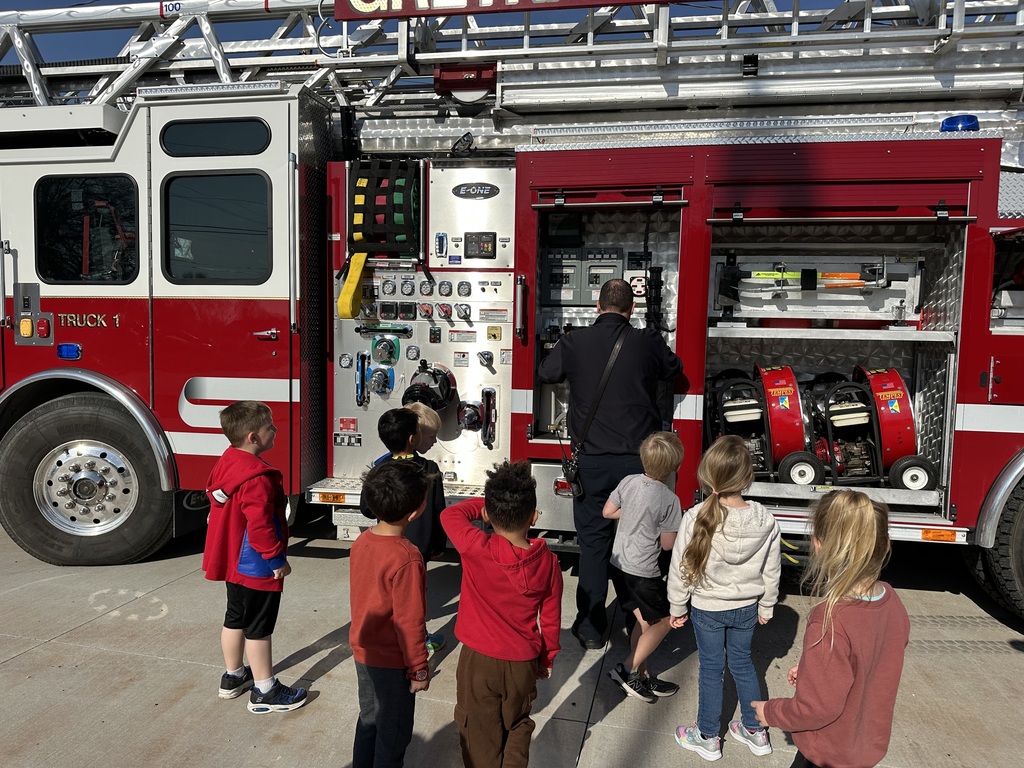 A group of children watch a firefighter who is showing off parts of a firetruck.