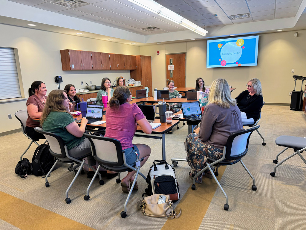 several GPS staff members sitting at a group of tables discussing with laptop open