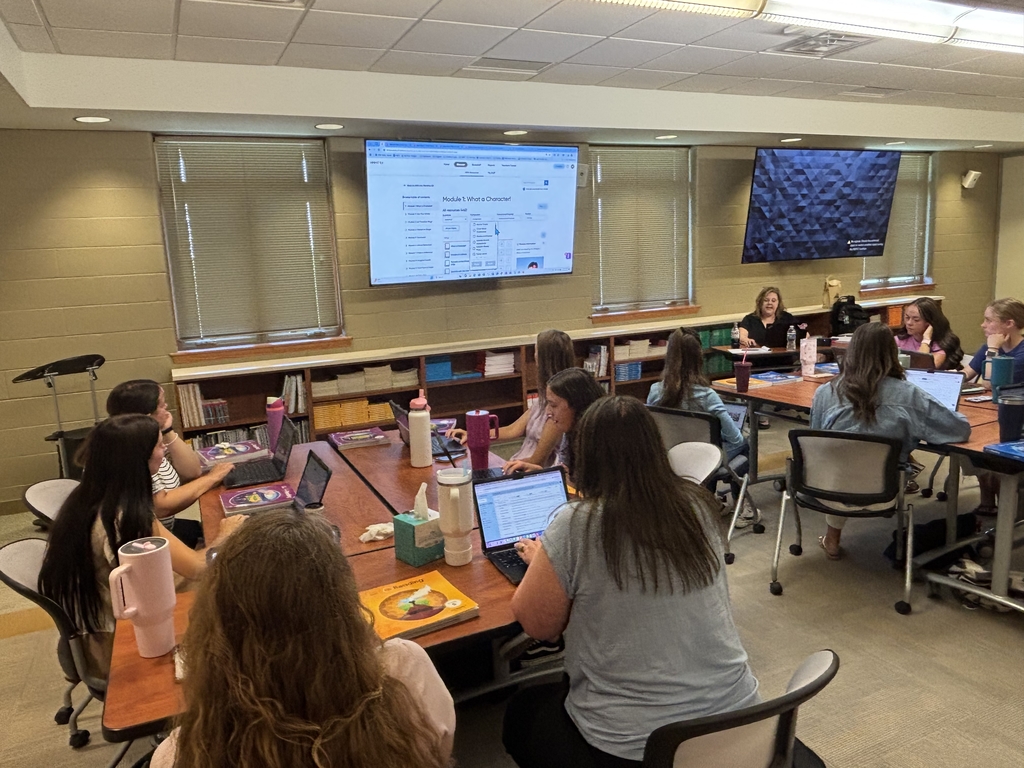 new staff at large tables grouped together looking at tv displaying video of math curriculum