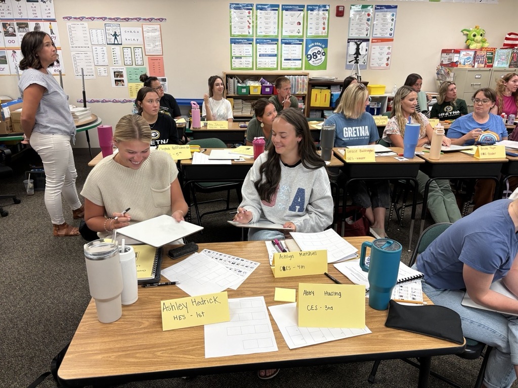 Large group of new teachers gathered for training on new reading techniques all smiles and collaborating between desks.
