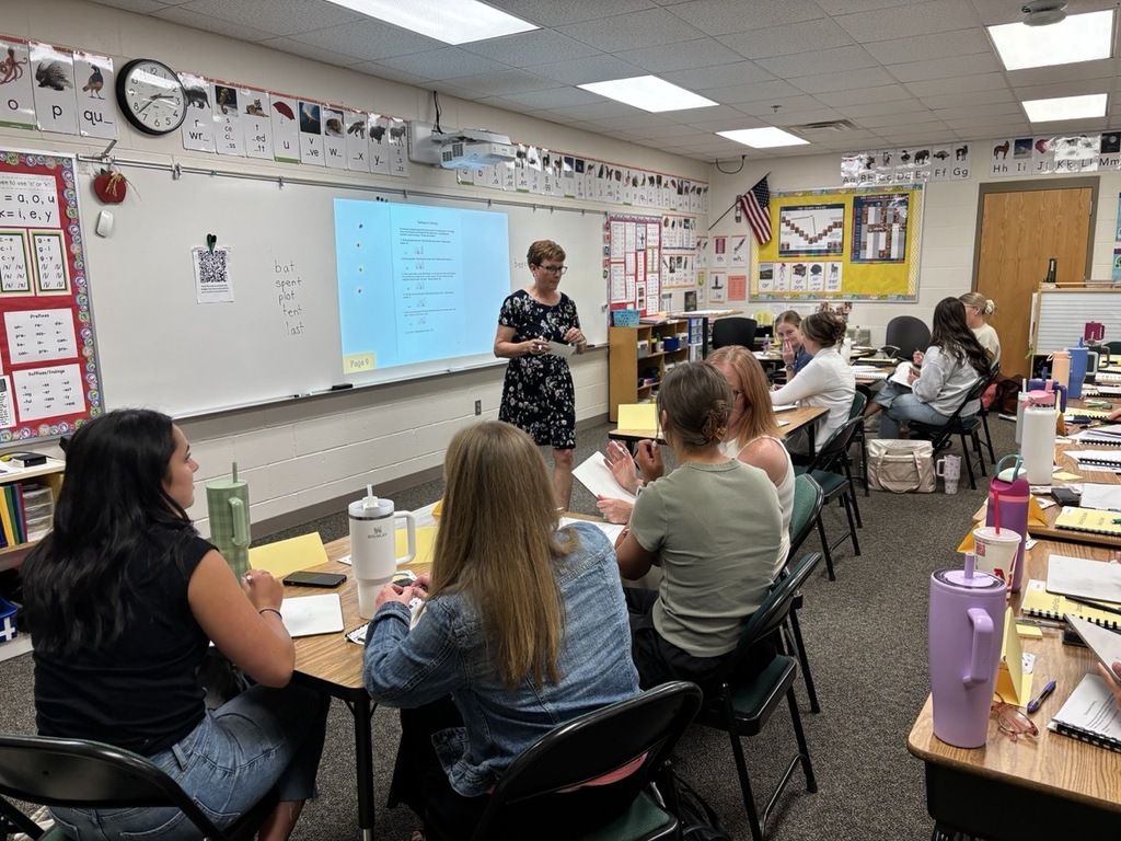 Presenter speaking to new teachers in front of classroom while staff is sitting at the student's desks