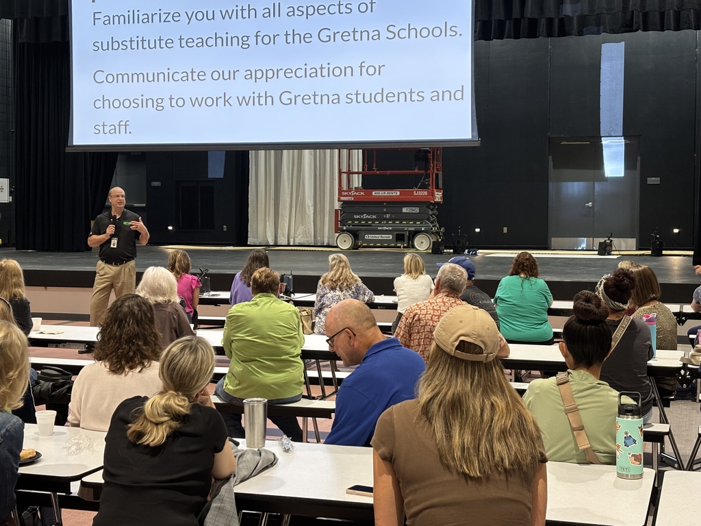 presenter speaking to new substitutes in the Giles Creek Middle school cafeteria with projector in background above stage.