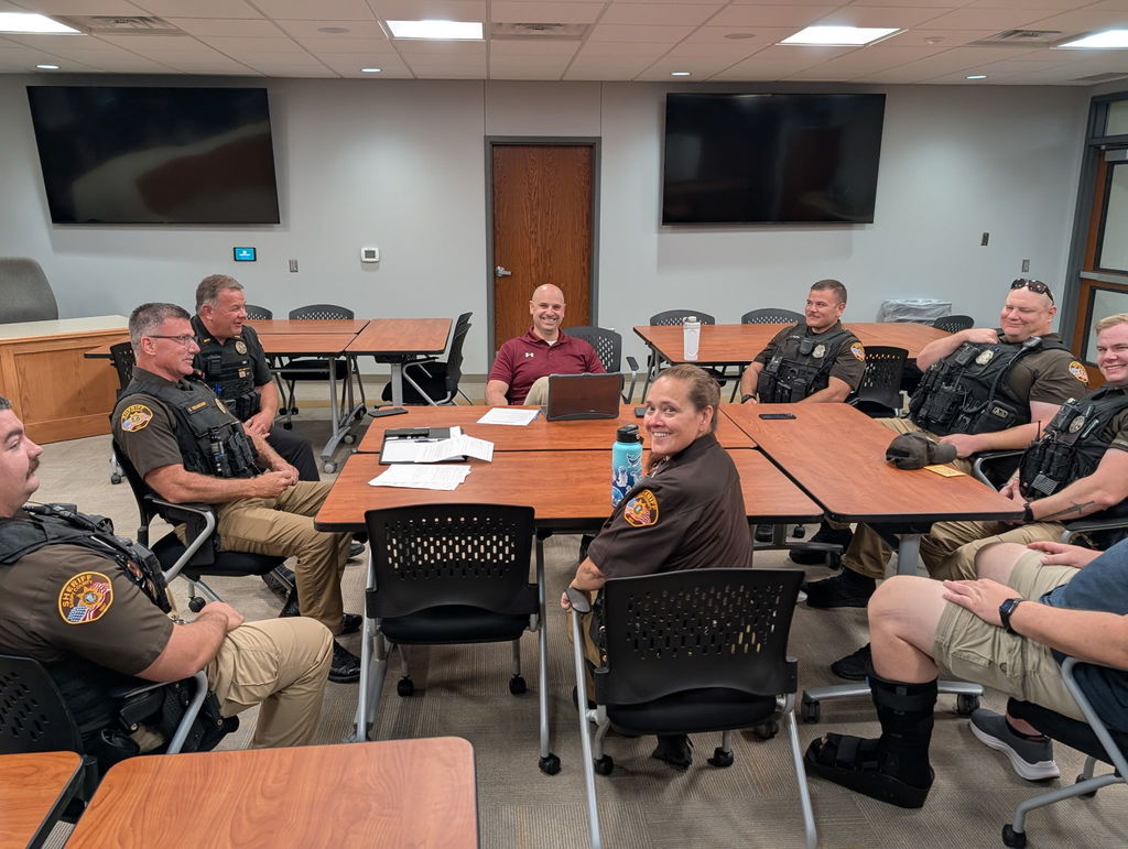 A large group of SRO and police officers surrounding a table at Gretna Public Schools district office all smiling at the camera