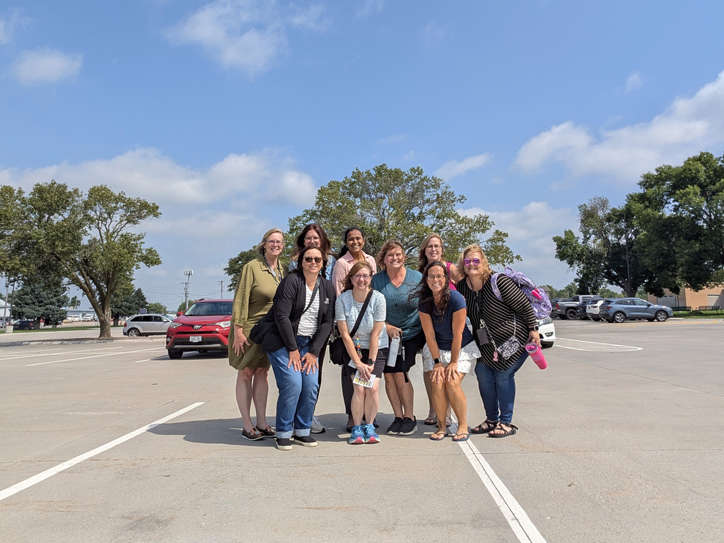 a group of nine district office staff members who are all smiles standing in the parking lot of the district office headed out to the all staff meeting