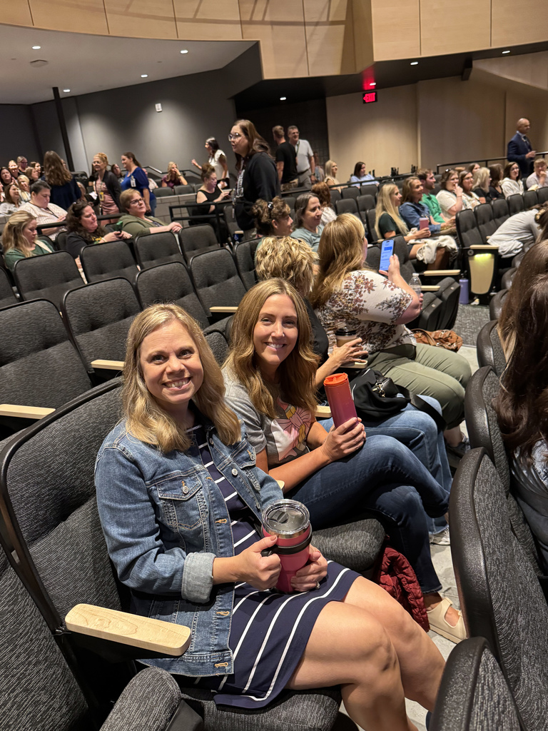 two staff members sitting in auditorium seating smiling at the camera