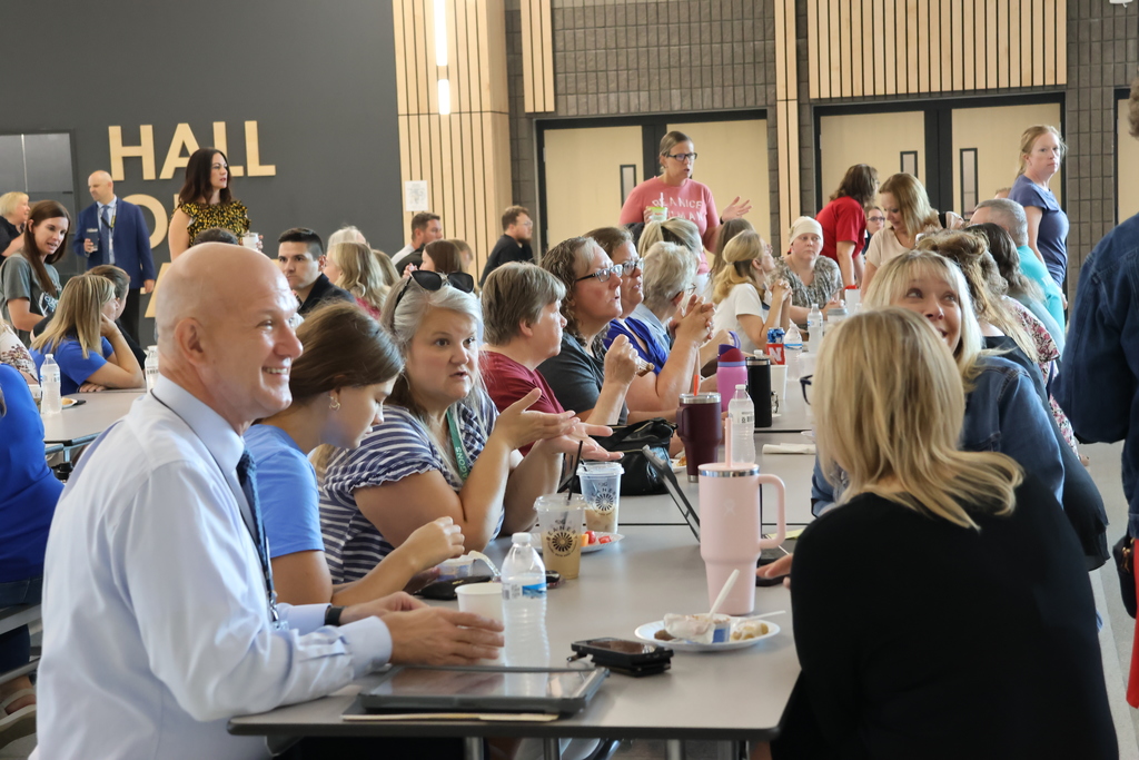 a long table in cafeteria filled with staff members laughing together and talking