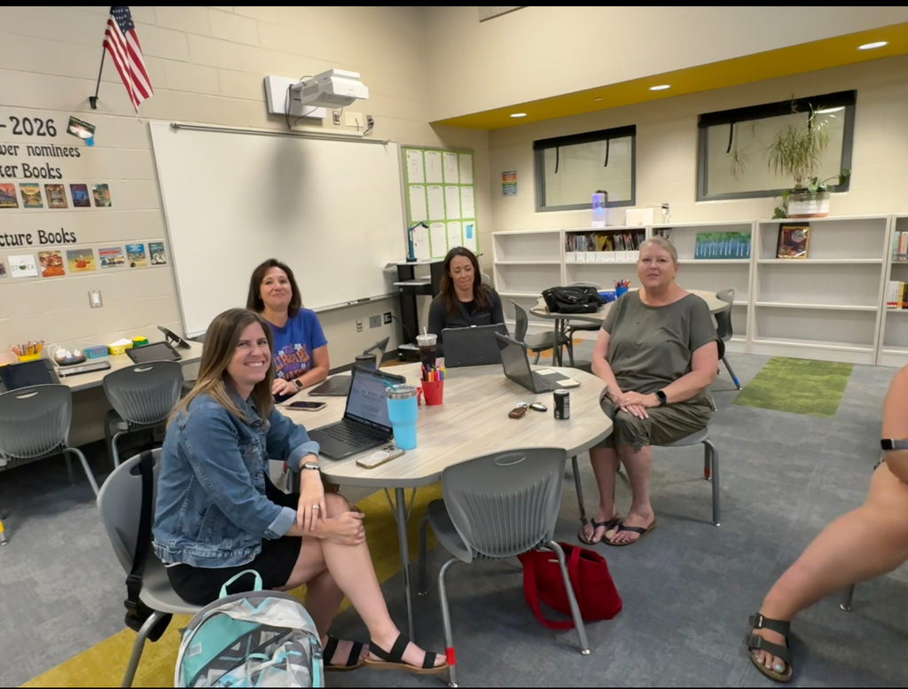 Elementary librarians sitting at a table in the library collaborating and smiling at the camera