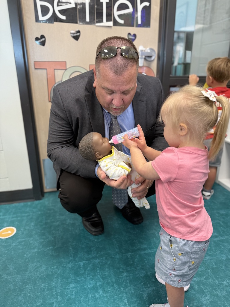 child feeding baby doll with a bottle while Superintendent Lightle holds it