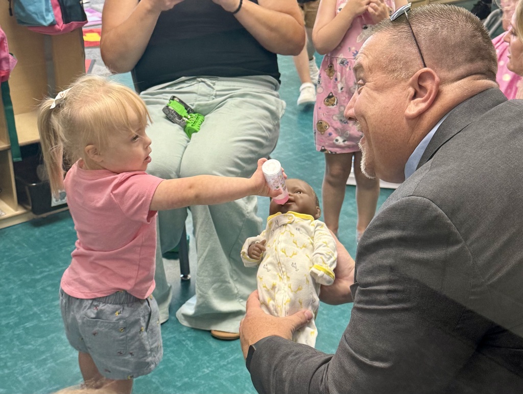 student feeding baby doll a bottle while Superintendent Lightle holds it