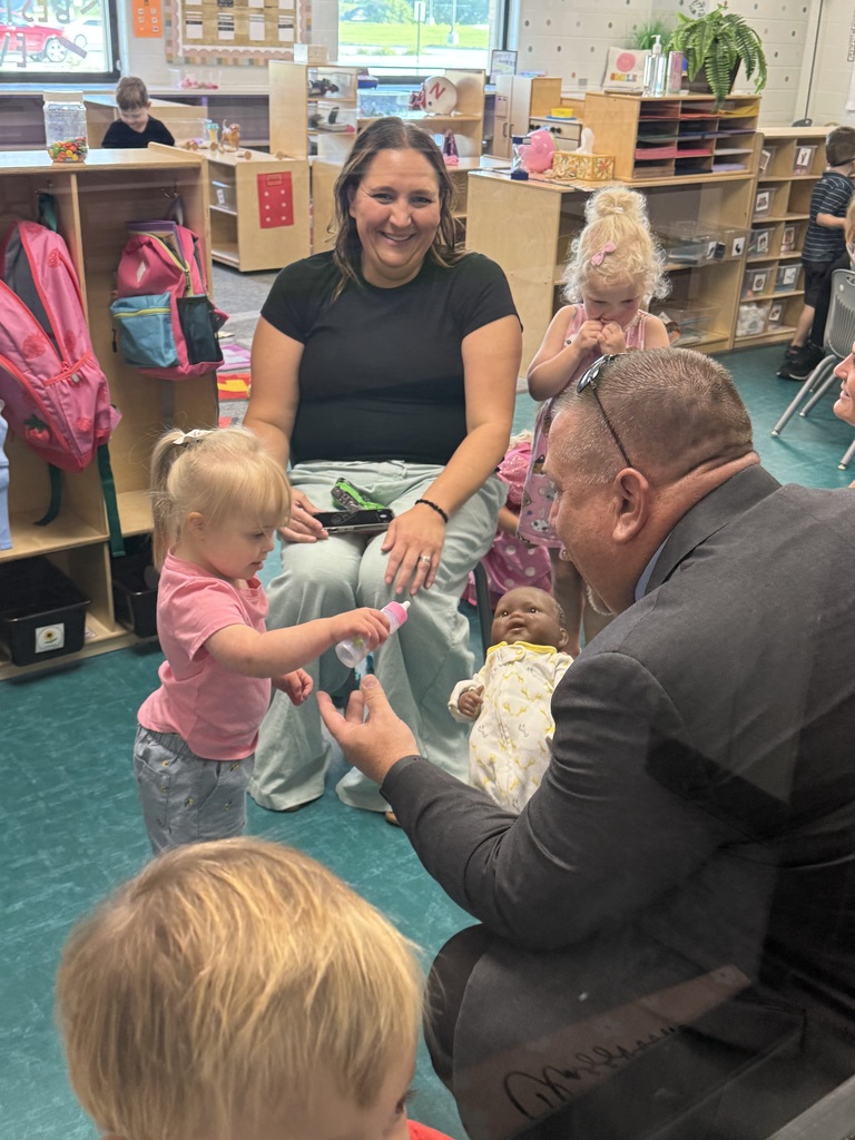 student giving bottle to a baby doll while teacher looks on