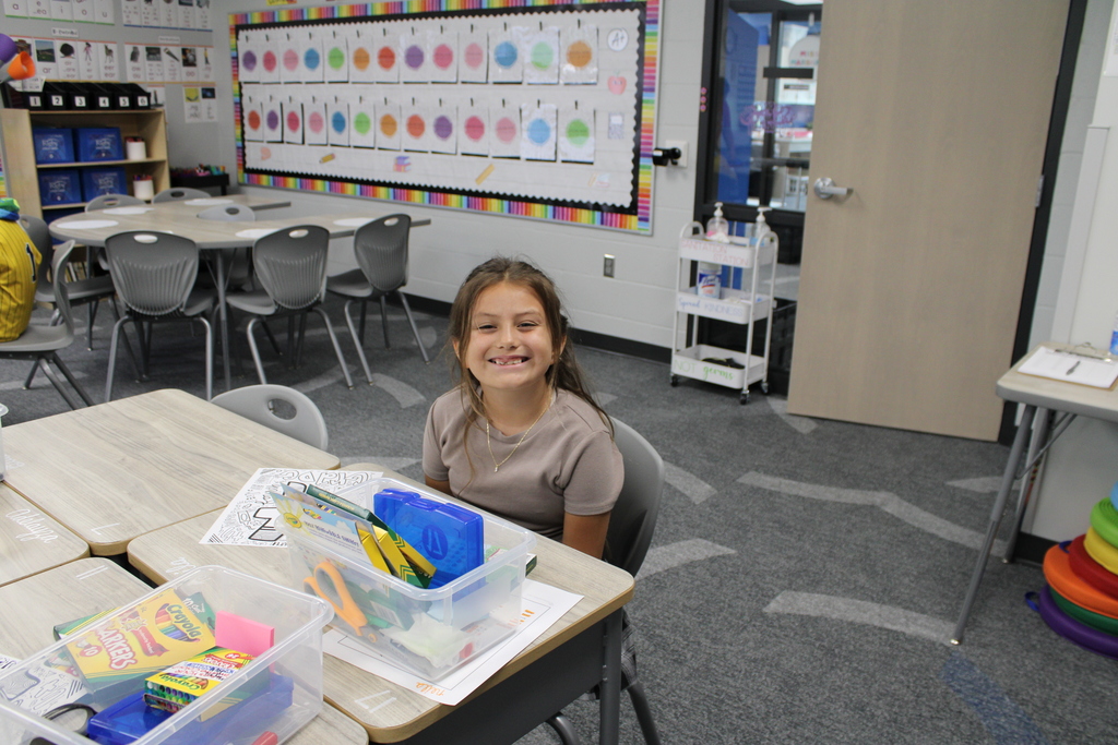 An eager student sits at her desk, ready for class with her colorful school supplies.