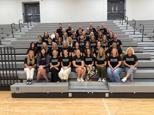 About thirty people wearing black posing for a picture on a bleacher