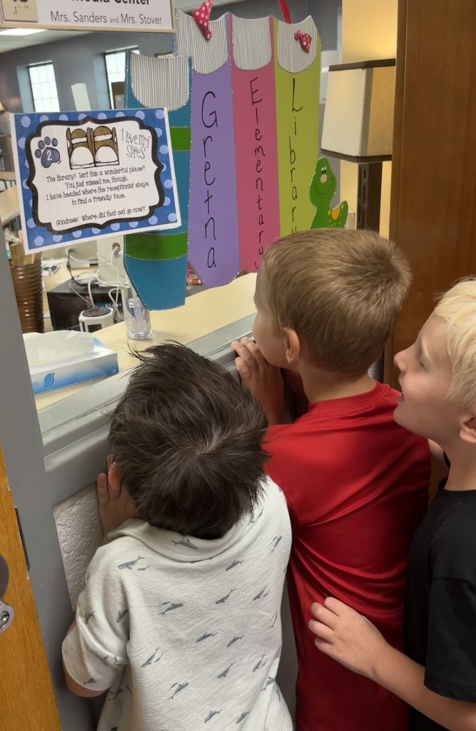 Three kids stand and look intently through a window.