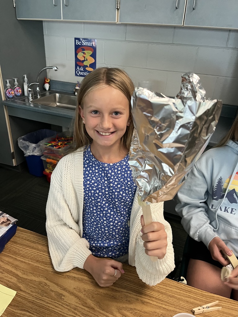 A girl wearing a blue shirt smiles while holding aluminum foil.