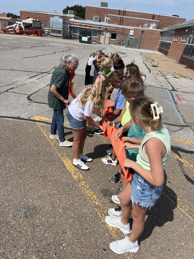A group of students and an adult stand in a row while holding a long piece of paper.