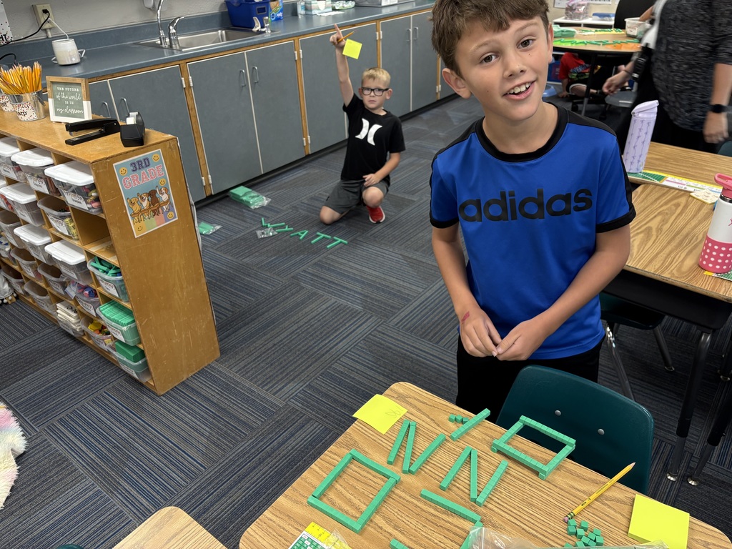 Student standing next to a desk that has green place value blocks.