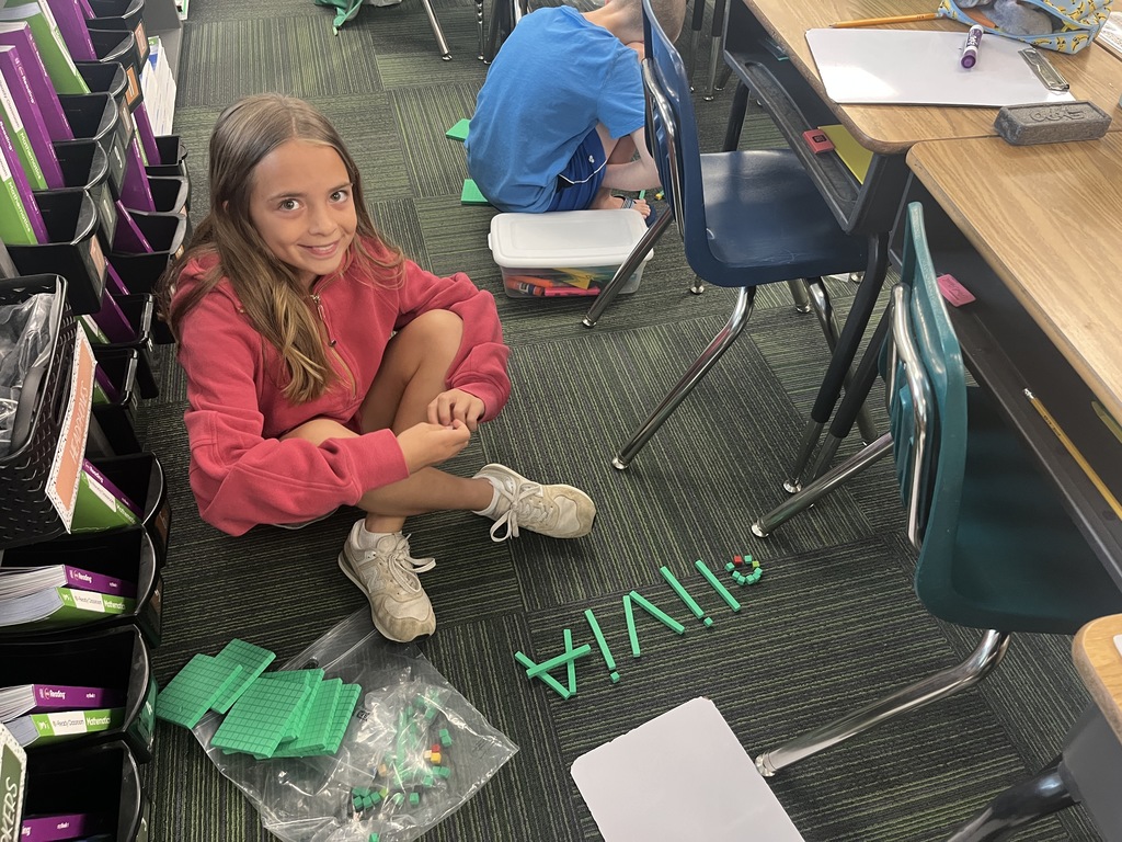 Girl smiling sitting on carpet with her name spelled out in place value blocks.