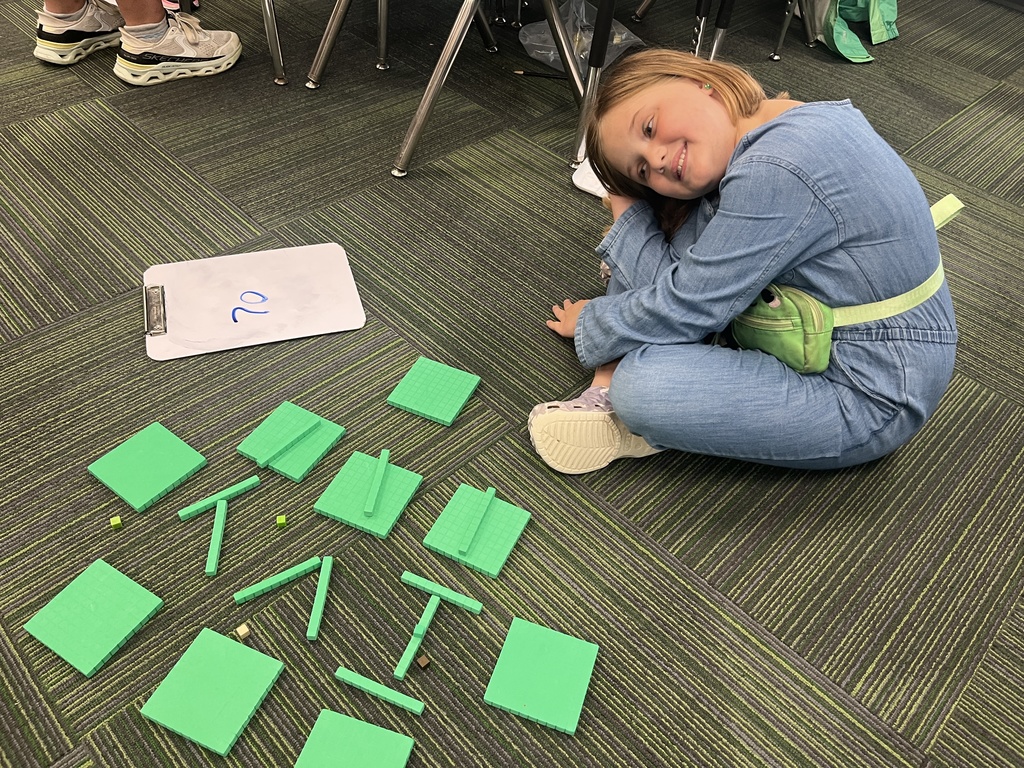 Girl smiling sitting on carpet with her name spelled out in place value blocks.
