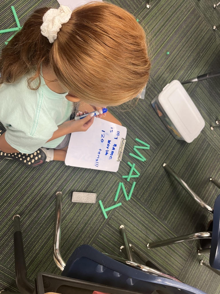 Girl sitting on carpet with her name spelled out in place value blocks.