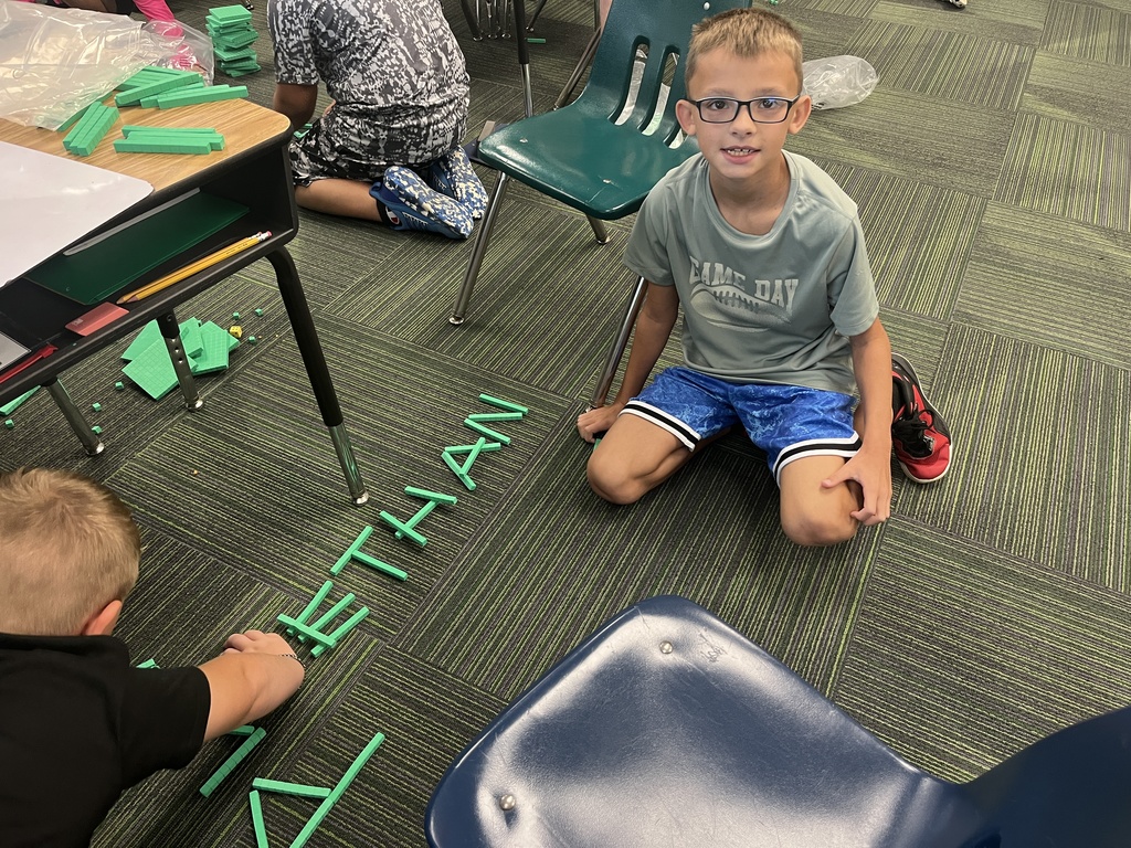 Boy smiling sitting on carpet with his name spelled out in place value blocks.