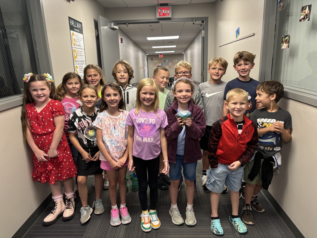 A group of young students stand in a hallway smiling.  One student holds a 3d printed gemstone.