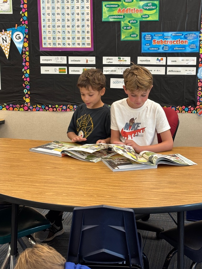 Two boys sitting at a table looking at picture books.
