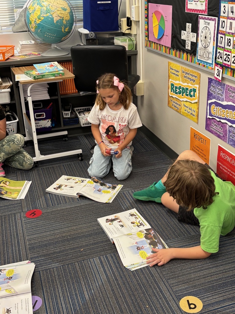 A boy and a girl sitting on the ground reading a picture book.