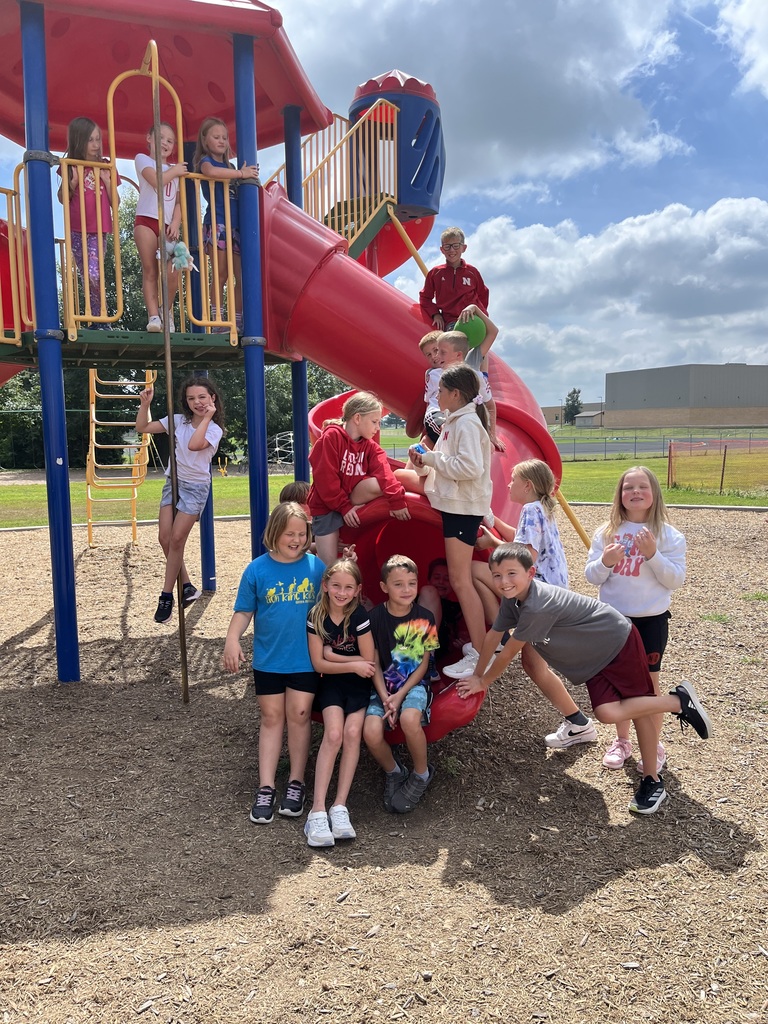 Children playing on a colorful playground with a large red spiral slide under a partly cloudy sky.