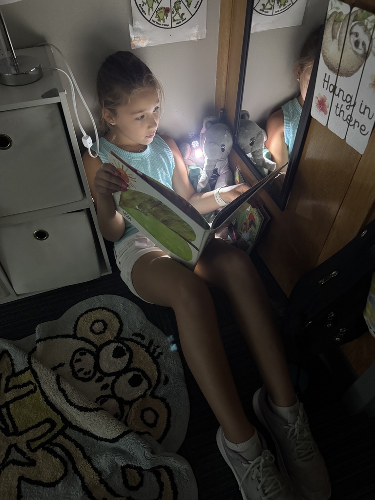 Student reading a book in the dark with a flashlight.