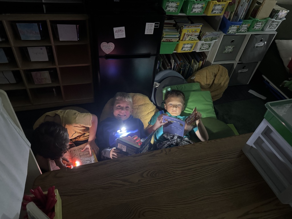 Three students reading a book in the dark with flashlights.