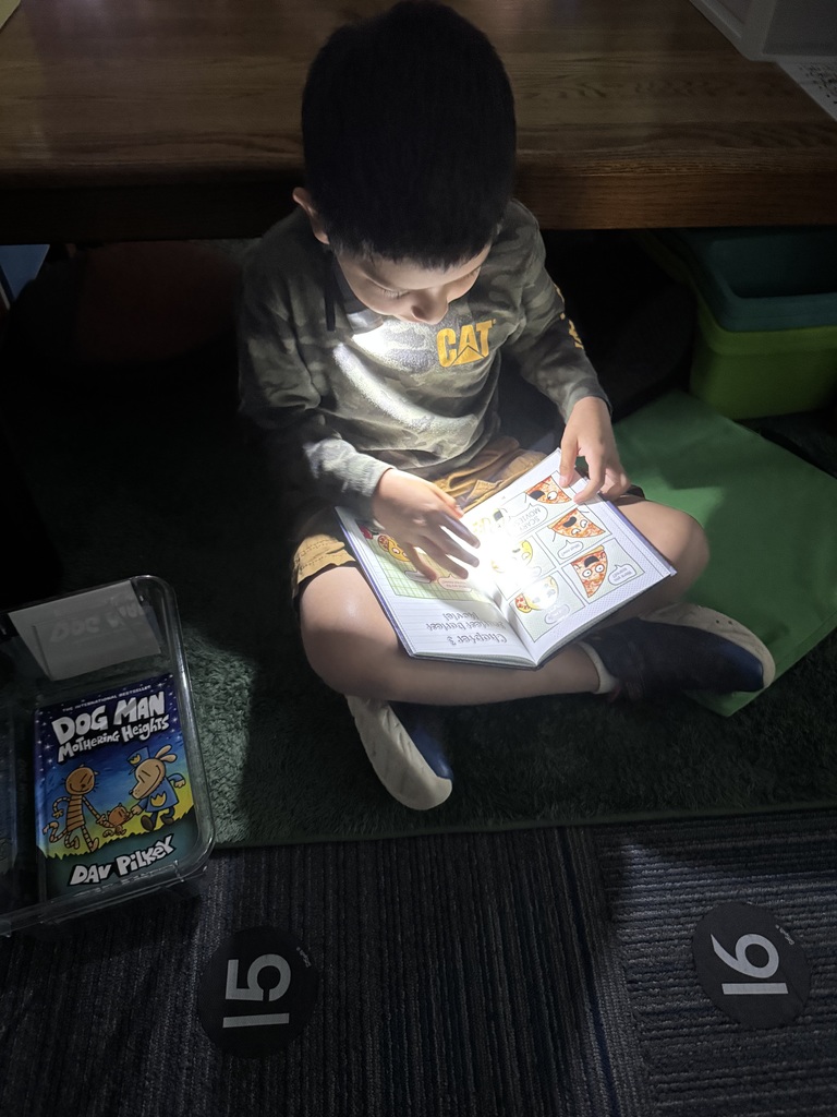Student reading a book in the dark with a flashlight.