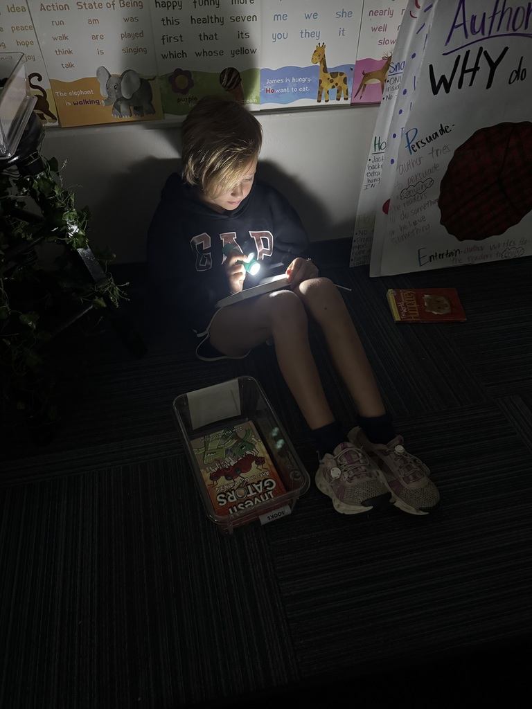 Student reading a book in the dark with a flashlight.