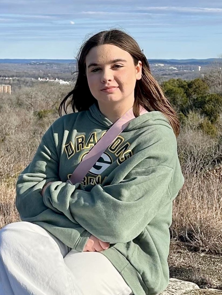 photo of a student sitting on a rock arms crossed with city behind