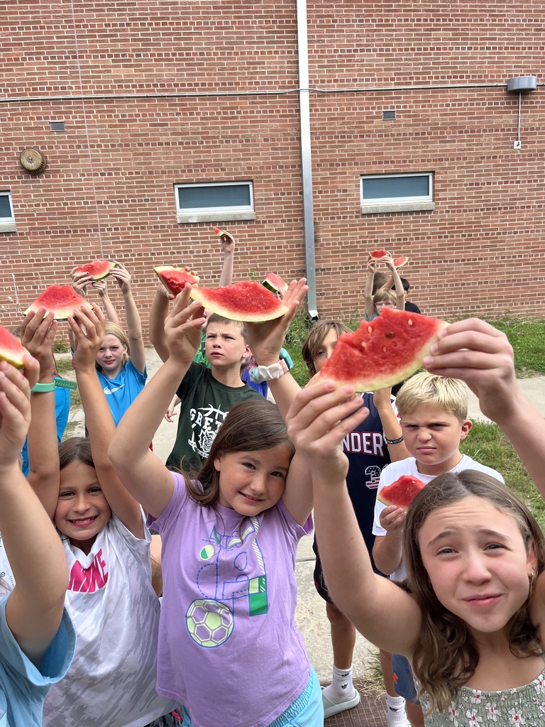 Group of students look at camera while holding up a watermelon slice as a pose.