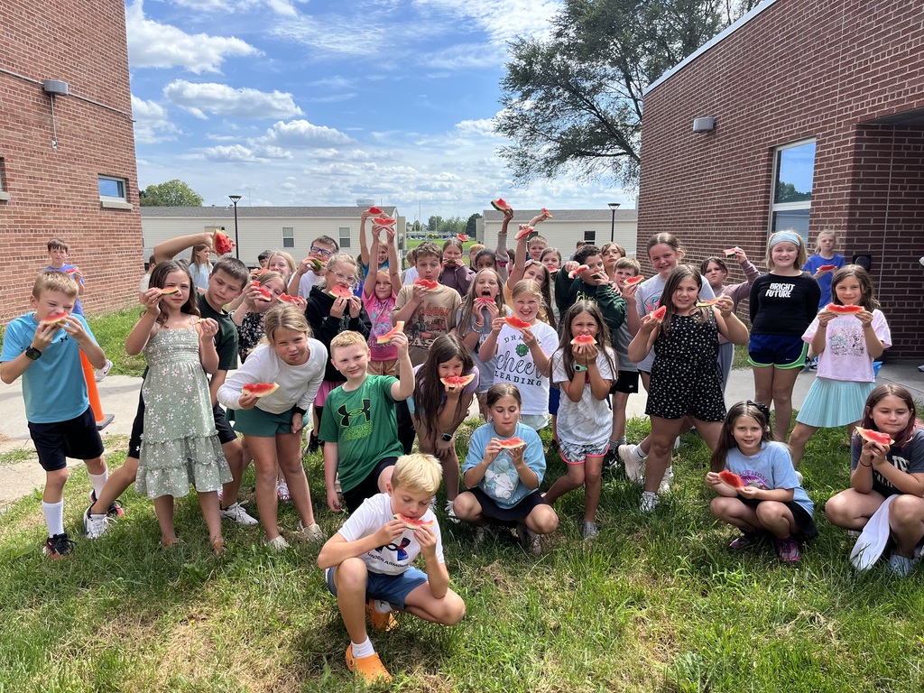 Group of students look at camera while holding up a watermelon slice as a pose.
