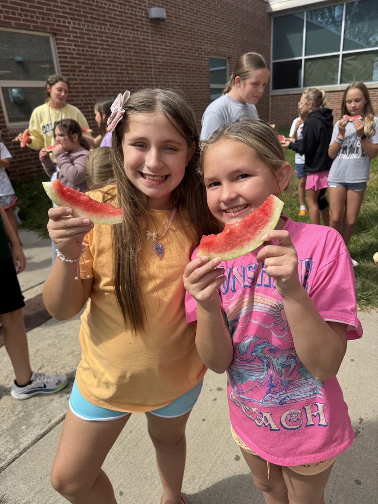 Two girls smile while holding a slice of watermelon each.