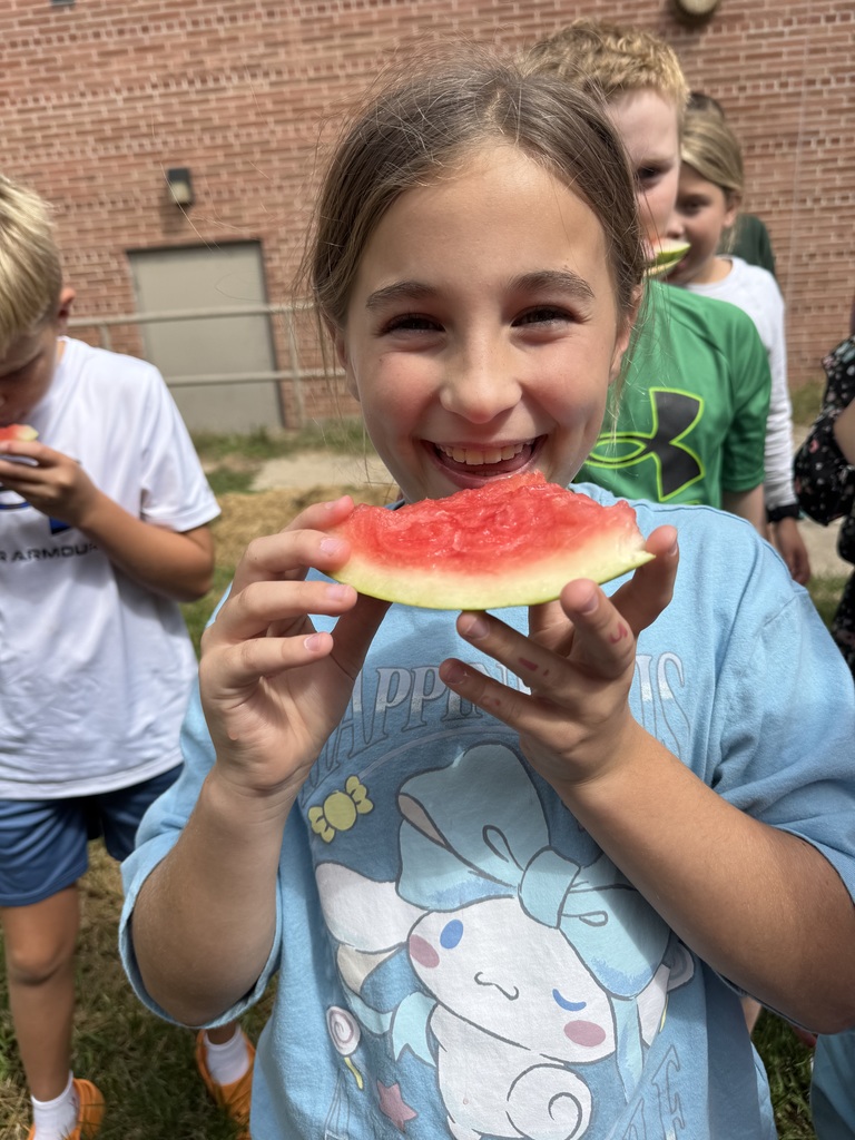Girl smiles while holding a slice of watermelon.