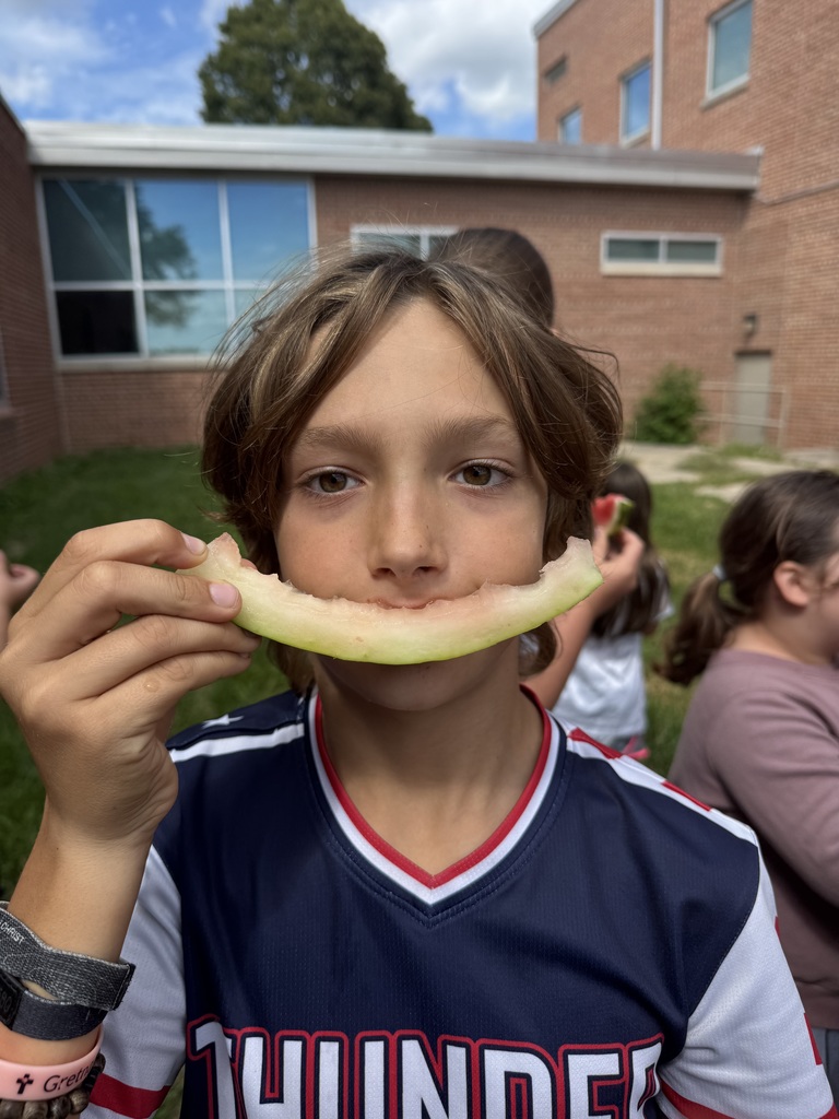 Boy holds what is left of a watermelon slice while looking at camera.