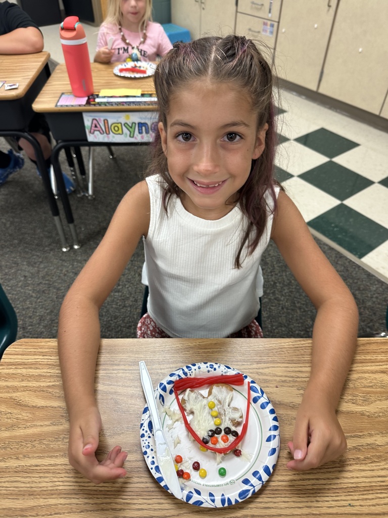 First grade student at desk smiling with gingerbread cookie