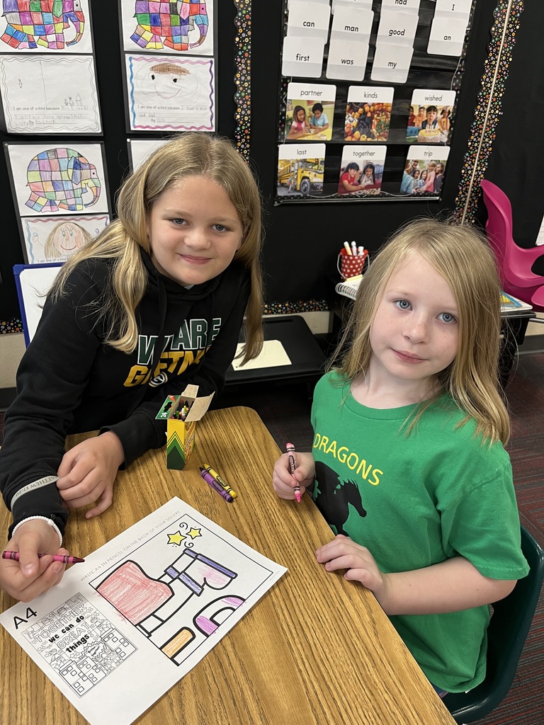 Two girls sitting at a desk with a coloring page in front of them.  They are both smiling.