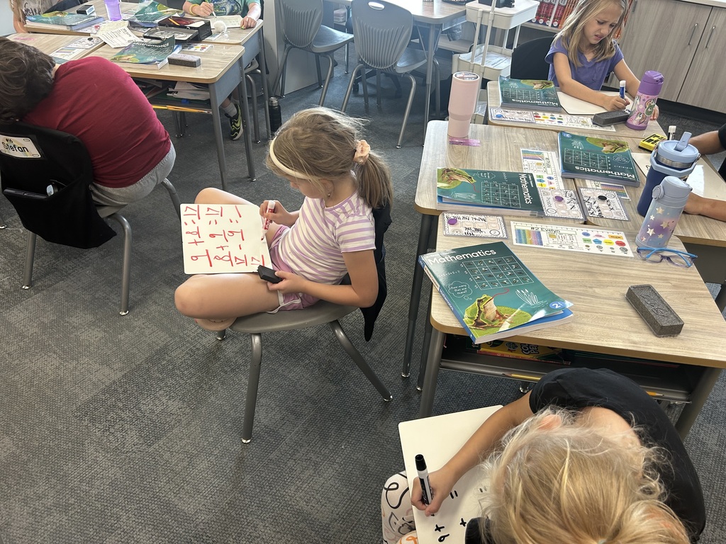 Mrs. Matousek and Mrs. Auman's 2nd grade students are working hard at math in a classroom at their seats using whiteboards. 
