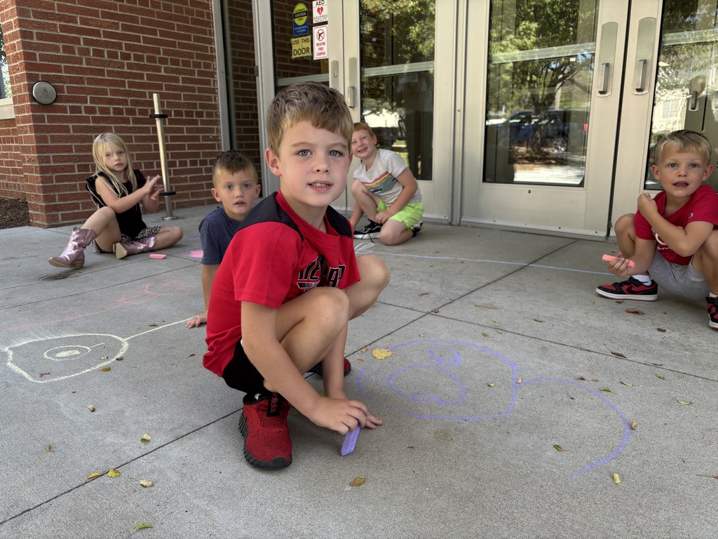 Four kids draw with sidewalk chalk on a sidewalk.