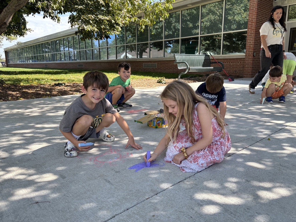 Four kids draw with sidewalk chalk on a sidewalk.