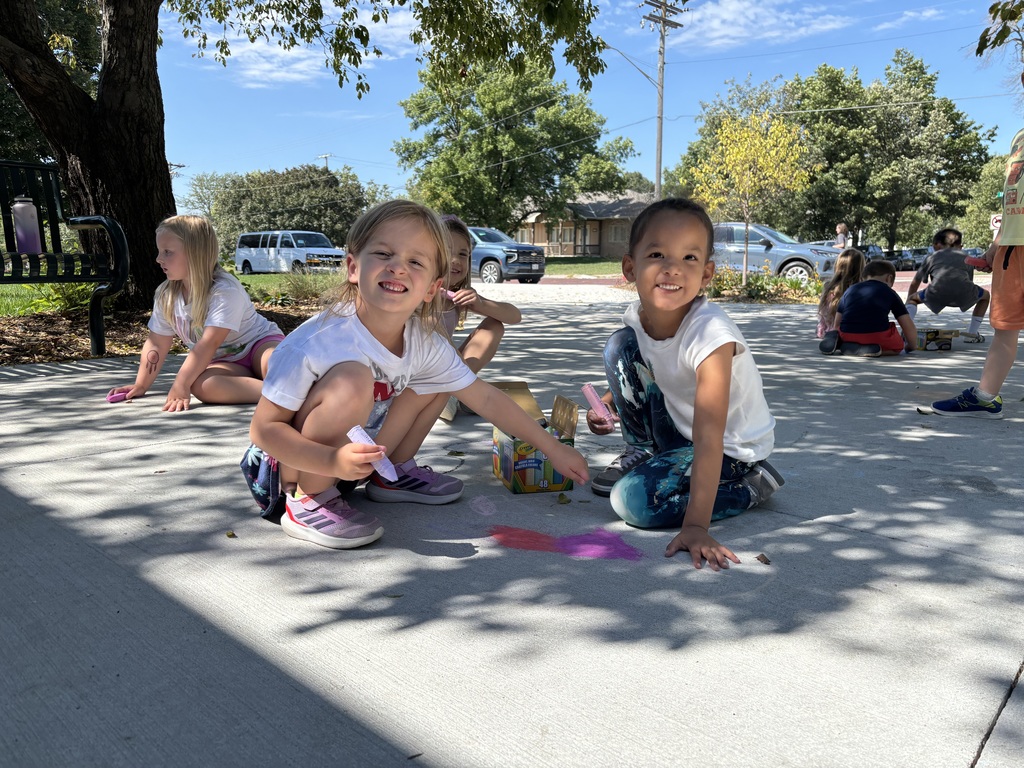 Four kids draw with sidewalk chalk on a sidewalk.